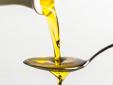 Close-Up Of Olive Oil Pouring On Spoon From Container Against White Background