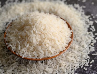 Milled rice in a bowl and a wooden spoon on the black cement floor. Selective focus